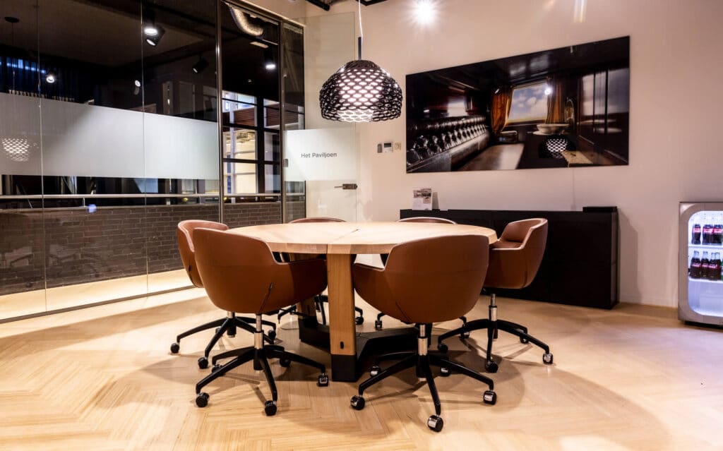 Vergaderruimte met ronde houten tafel, bruine bureaustoelen, glazen wanden en hanglamp bij Frame Offices.