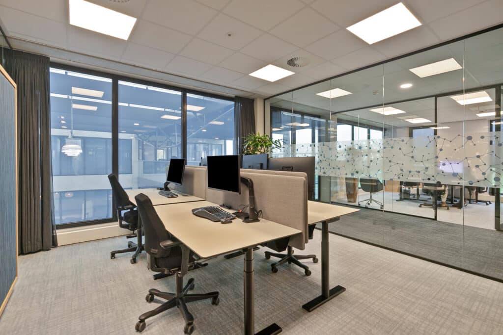 Kantoorruimte in Alphen a/d Rijn met bureaus, computerschermen, bureaustoelen en glazen wanden.