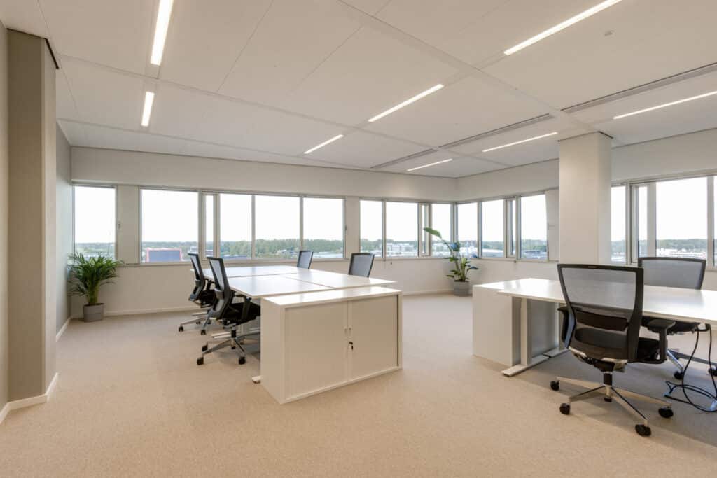 Kantoorruimte in Gaudi Amsterdam met meerdere bureaus, bureaustoelen, witte opbergkast, grote ramen en veel daglicht.