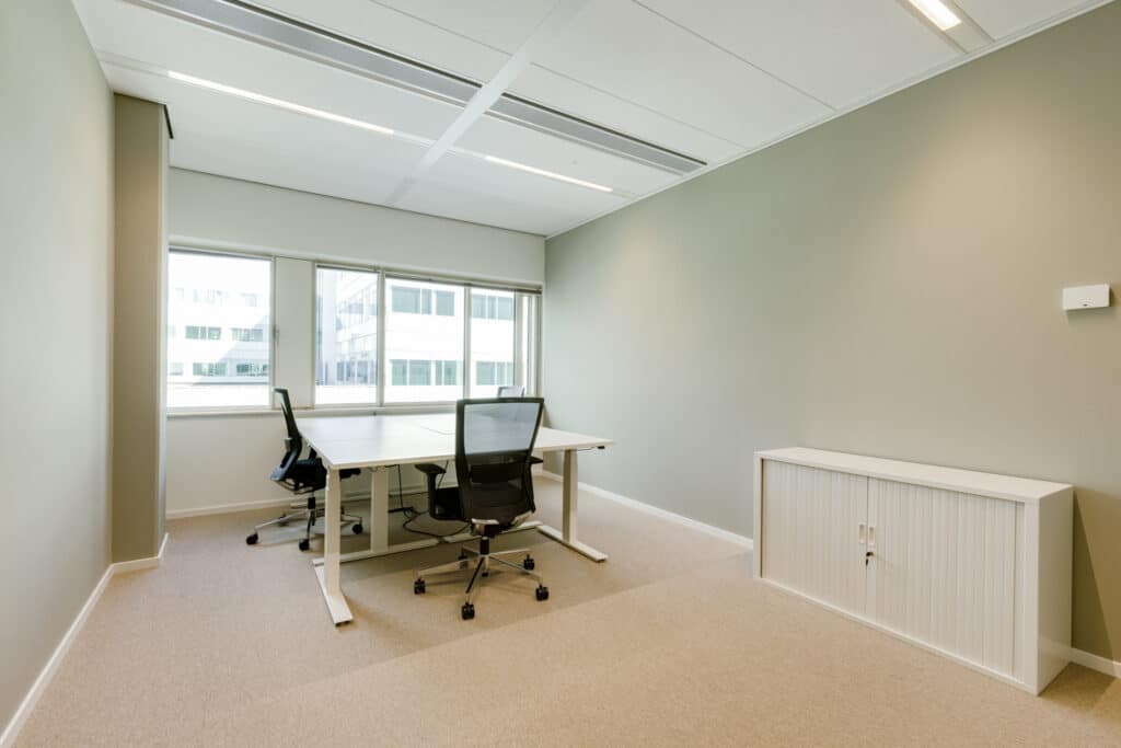 Kantoorruimte in Gaudi Amsterdam met twee bureaus, bureaustoelen, witte opbergkast en grote ramen.