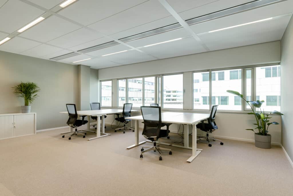 Kantoorruimte in Utrecht met witte bureaus, zwarte bureaustoelen, grote ramen, opbergkast en planten.