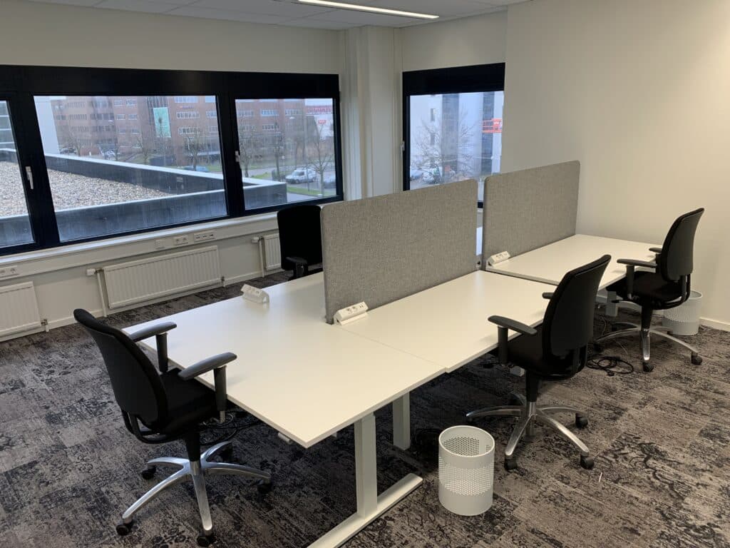 Kantoorruimte in Utrecht met witte bureaus, bureaustoelen, scheidingswanden en grote ramen met uitzicht op de stad.